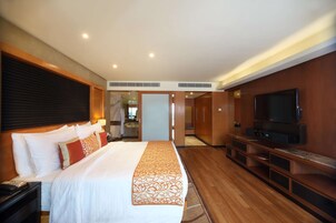 A hotel room with a large bed, a TV, and a wooden floor.