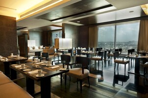 A modern hotel dining area with tables set for dining, large windows offering a city view, and a contemporary interior design.