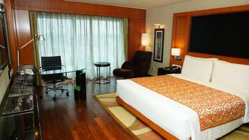 A hotel room with a large bed, a desk with a chair, a small table, and a lamp.