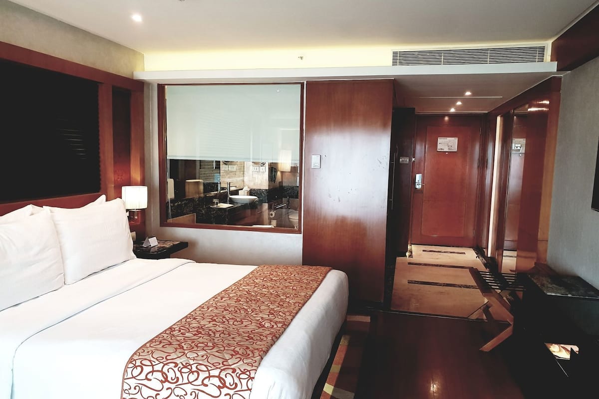 Habitación de hotel con una cama grande, un espejo, un escritorio y vistas al baño.