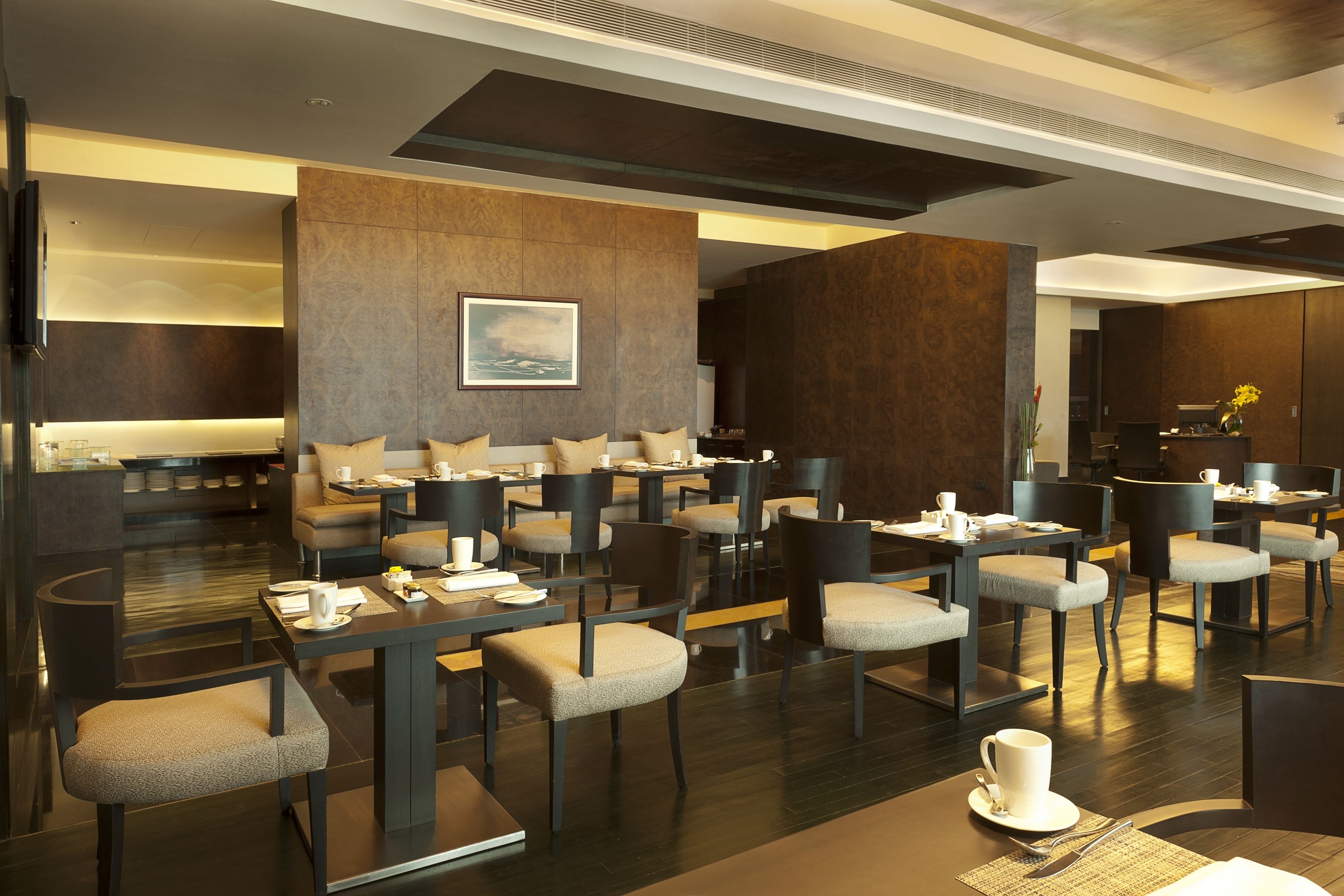 A modern hotel lobby with multiple seating areas, including sofas and tables. There are several chairs and a few tables with cups and saucers.