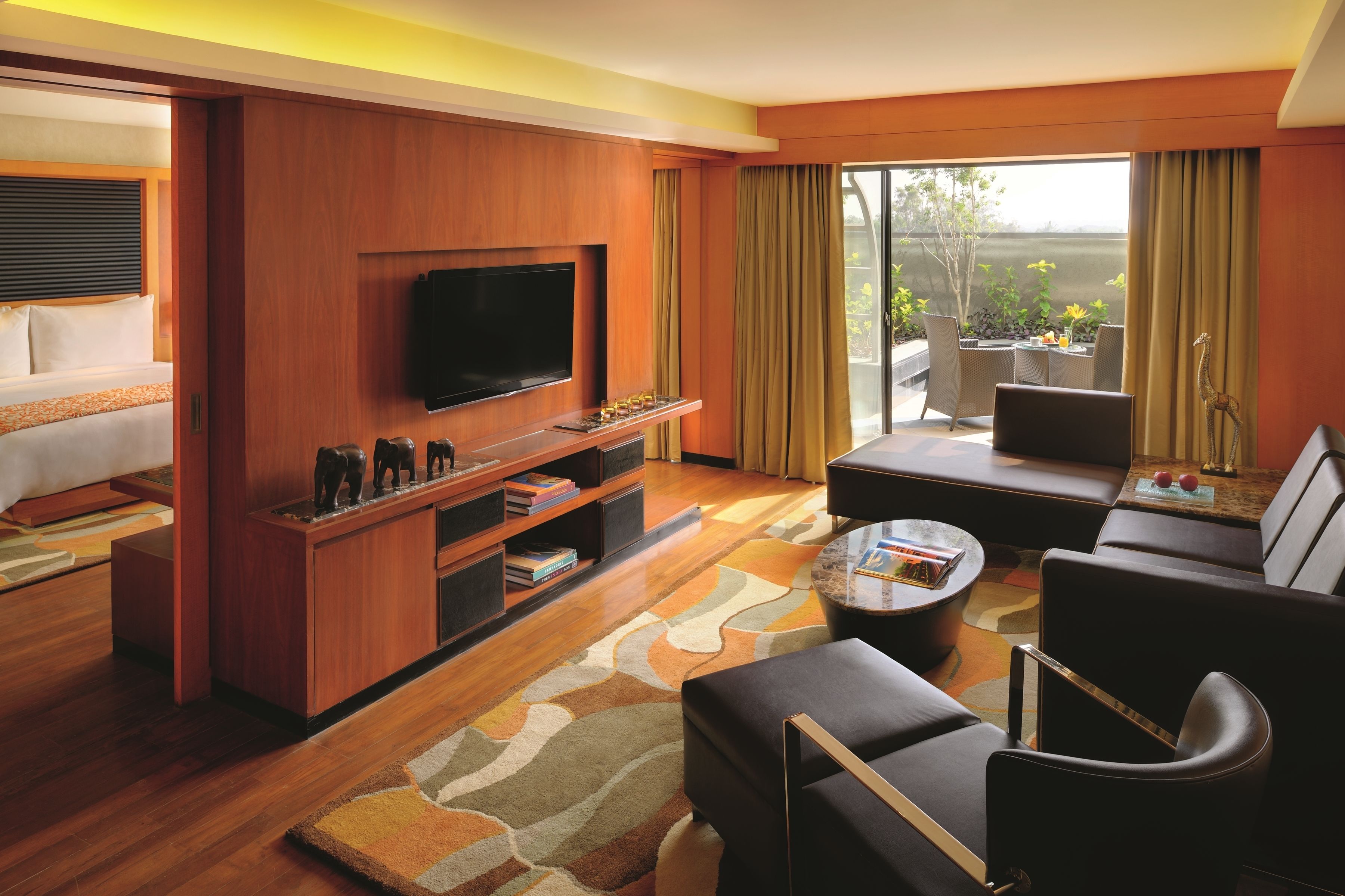 Una habitación de hotel moderna con televisión de pantalla plana, sofá, mesa de centro y balcón con mobiliario de exterior.