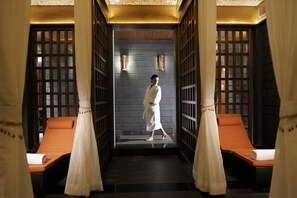 A spa room with a person in a robe, two massage chairs, and a dark wall with a wooden grid pattern. - Gokulam Grand Hotel & Spa Bangalore (Bengaluru)