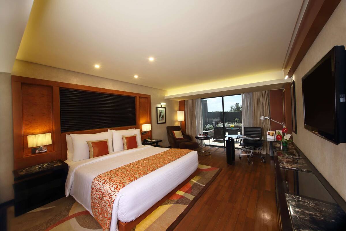 A hotel room with a large bed, a desk, a chair, a TV, and a view of the outdoors.