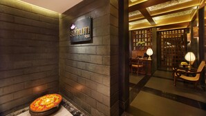 Un área de spa con un letrero que dice "Schum Spa", una pared de piedra, un baño de piedra climatizado y una zona de recepción con un mostrador y sillas.