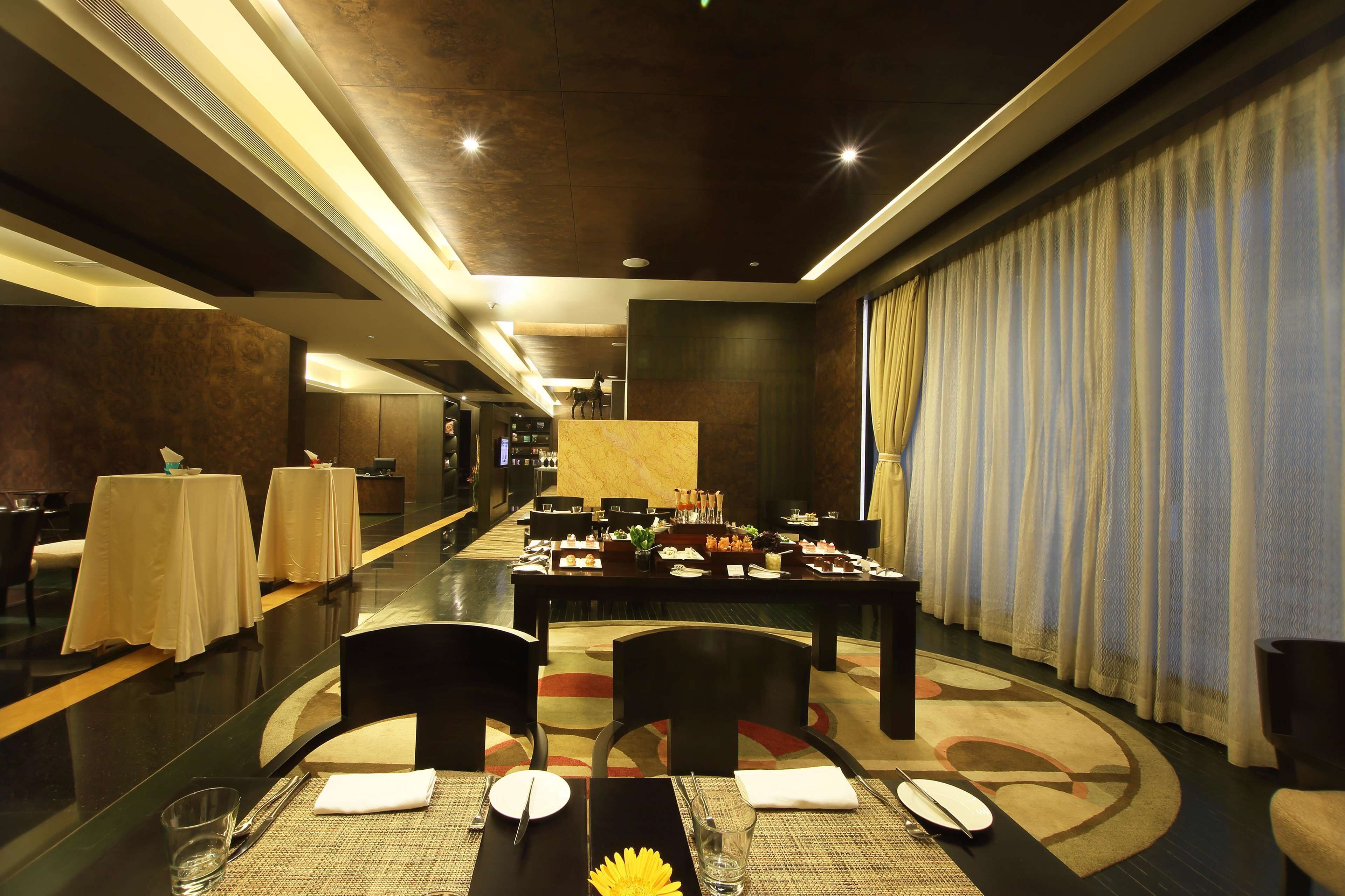 A modern dining area with tables set for a meal, a long corridor, and a large window with curtains.