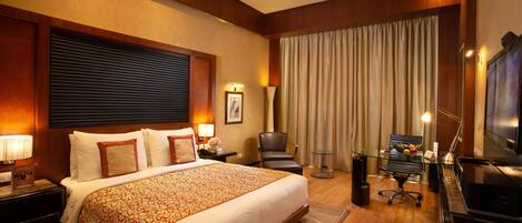 A hotel room with a large bed, a desk with a computer, a chair, and a TV.