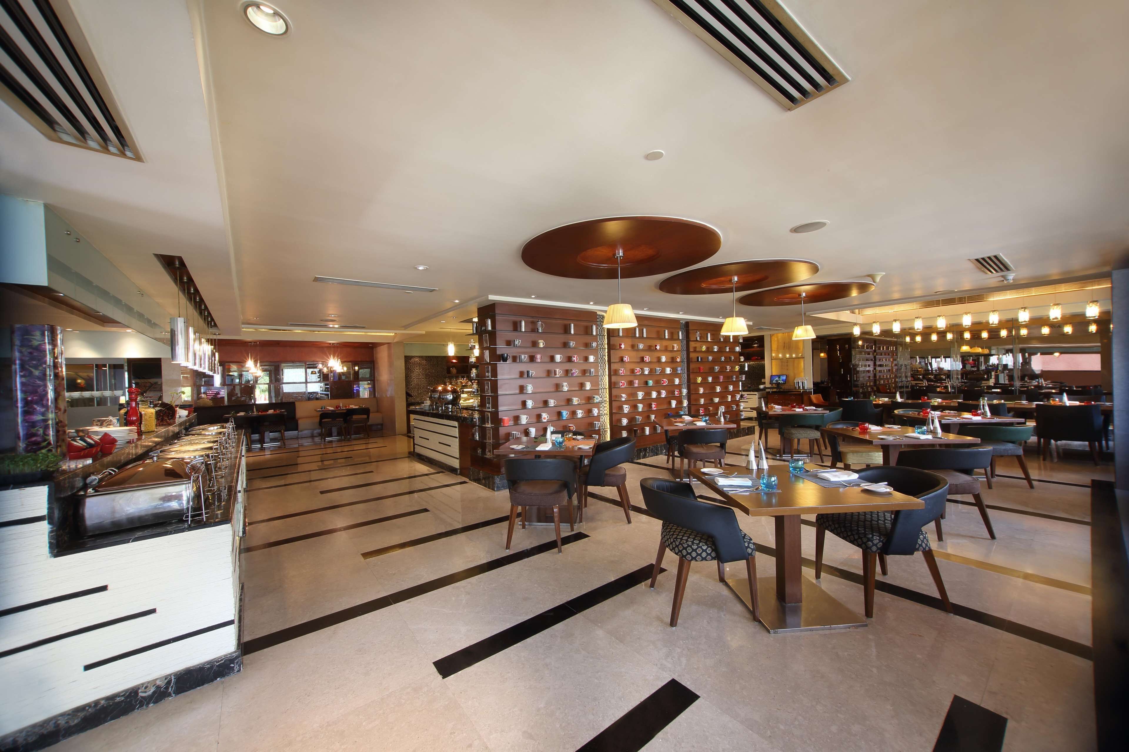 A spacious hotel lobby with multiple dining areas, a reception desk, and a wall displaying various items.