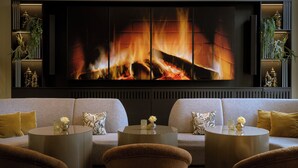 A modern living room with a fireplace, sofas, and round coffee tables. - Leonardo Royal Hotel Munich (Munich)