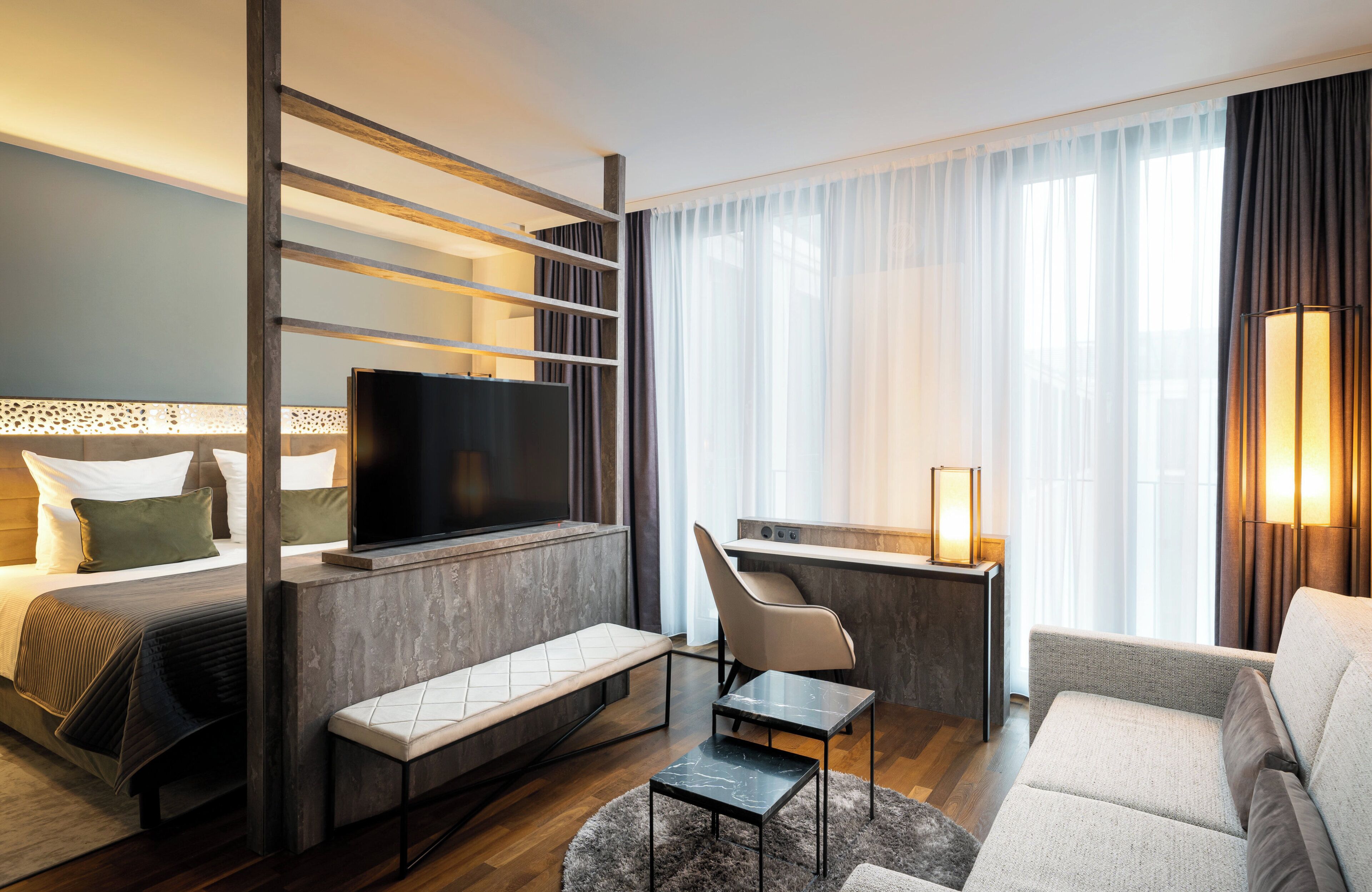 Una habitación de hotel moderna con cama, escritorio, televisor, sofá y sillón.
