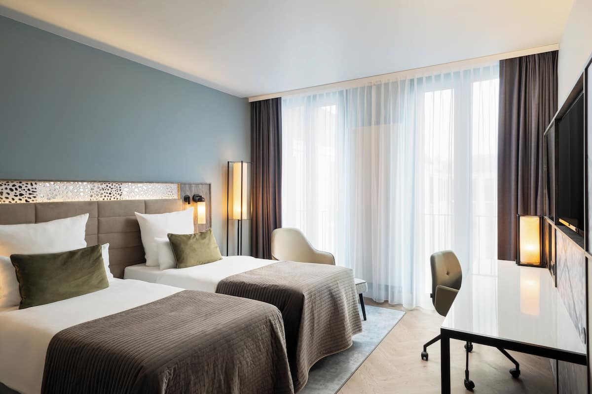 A hotel room with two beds, a desk, a chair, and a TV.