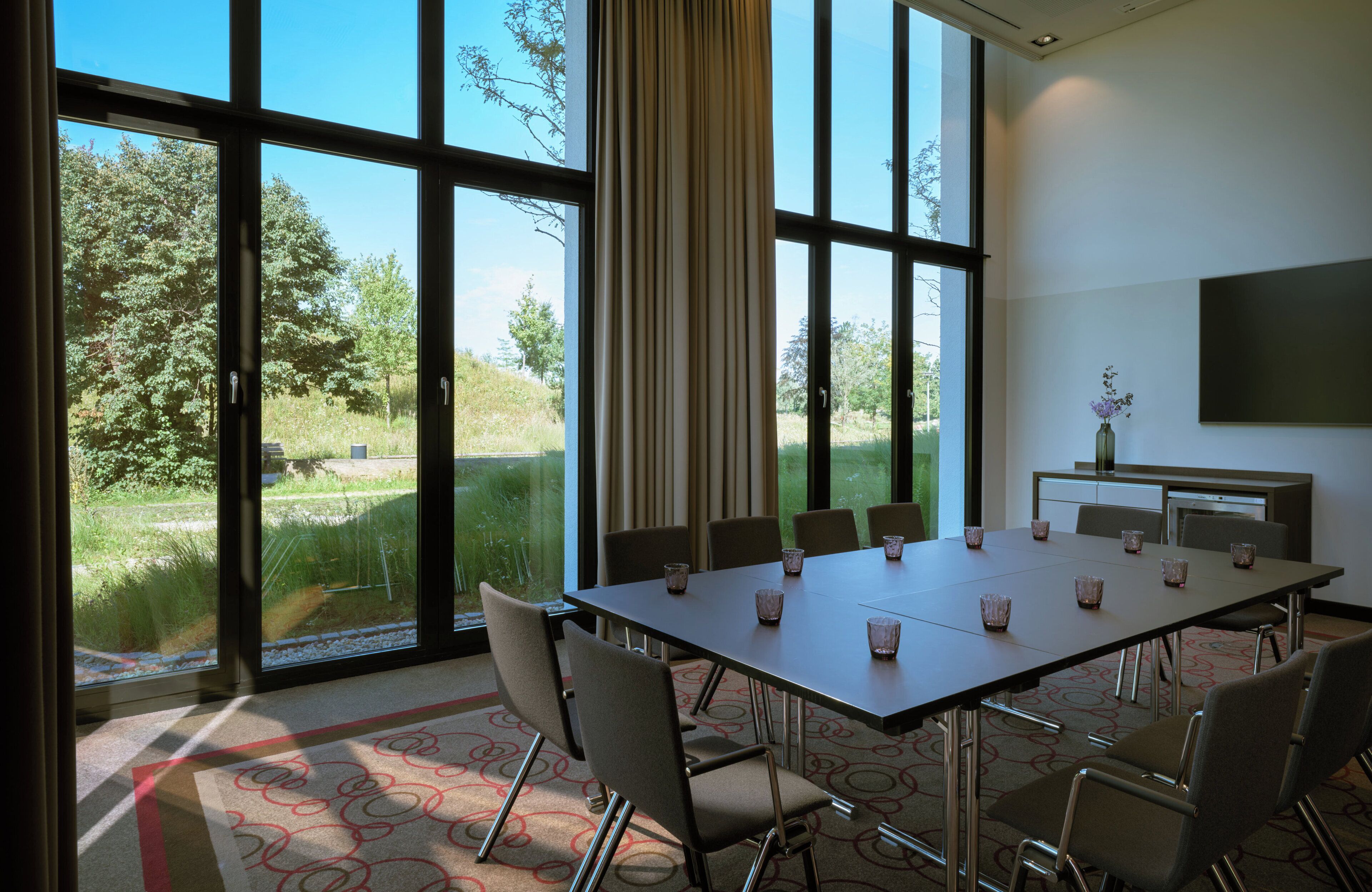 Un salón de conferencias con una mesa grande, sillas y una pantalla de televisión.