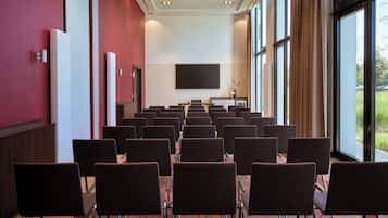 A conference room with rows of chairs, a large screen, and a view of the outdoors through large windows.