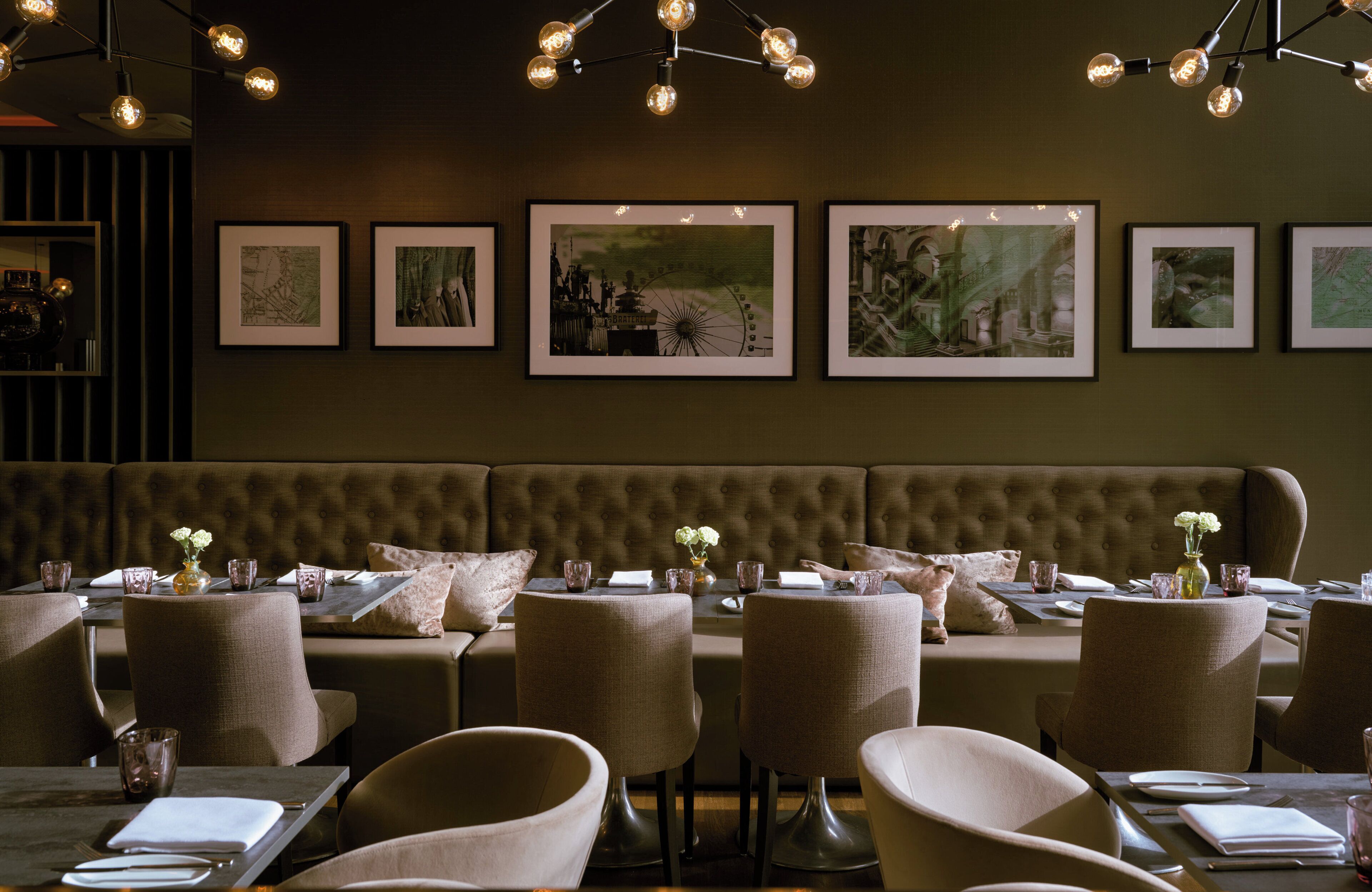 A restaurant with a tufted booth seating area, framed artwork on the wall, and pendant lighting.