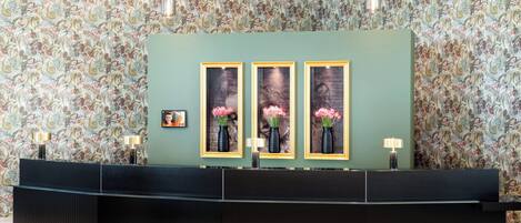 Un mostrador de recepción con tres obras de arte enmarcadas, un fondo de papel tapiz estampado y una moderna barra negra.