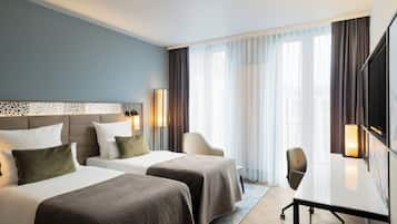 A hotel room with two beds, a desk, a chair, and a TV.
