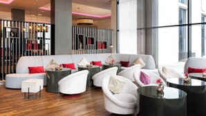 A modern lounge area with a grey sofa, white armchairs, and round tables. - Leonardo Royal Hotel Munich (Munich)