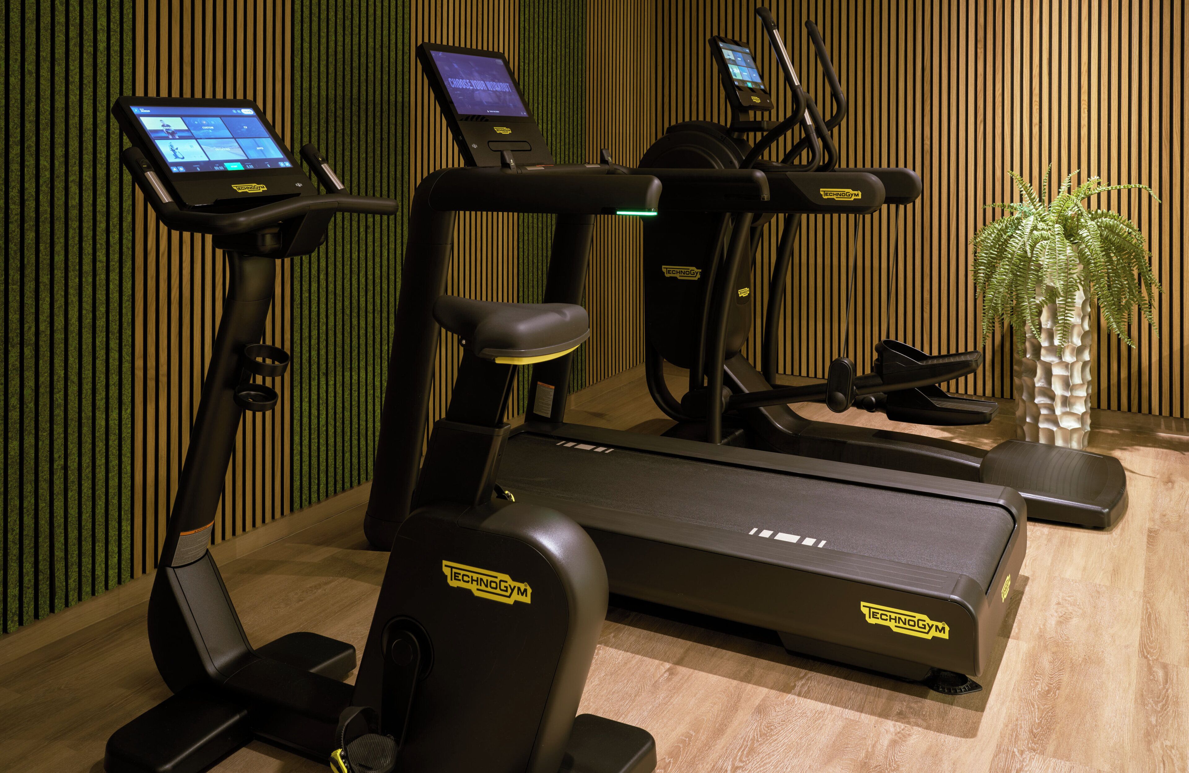 A gym with various exercise machines, including treadmills and elliptical trainers, and a digital interface for workout programs.