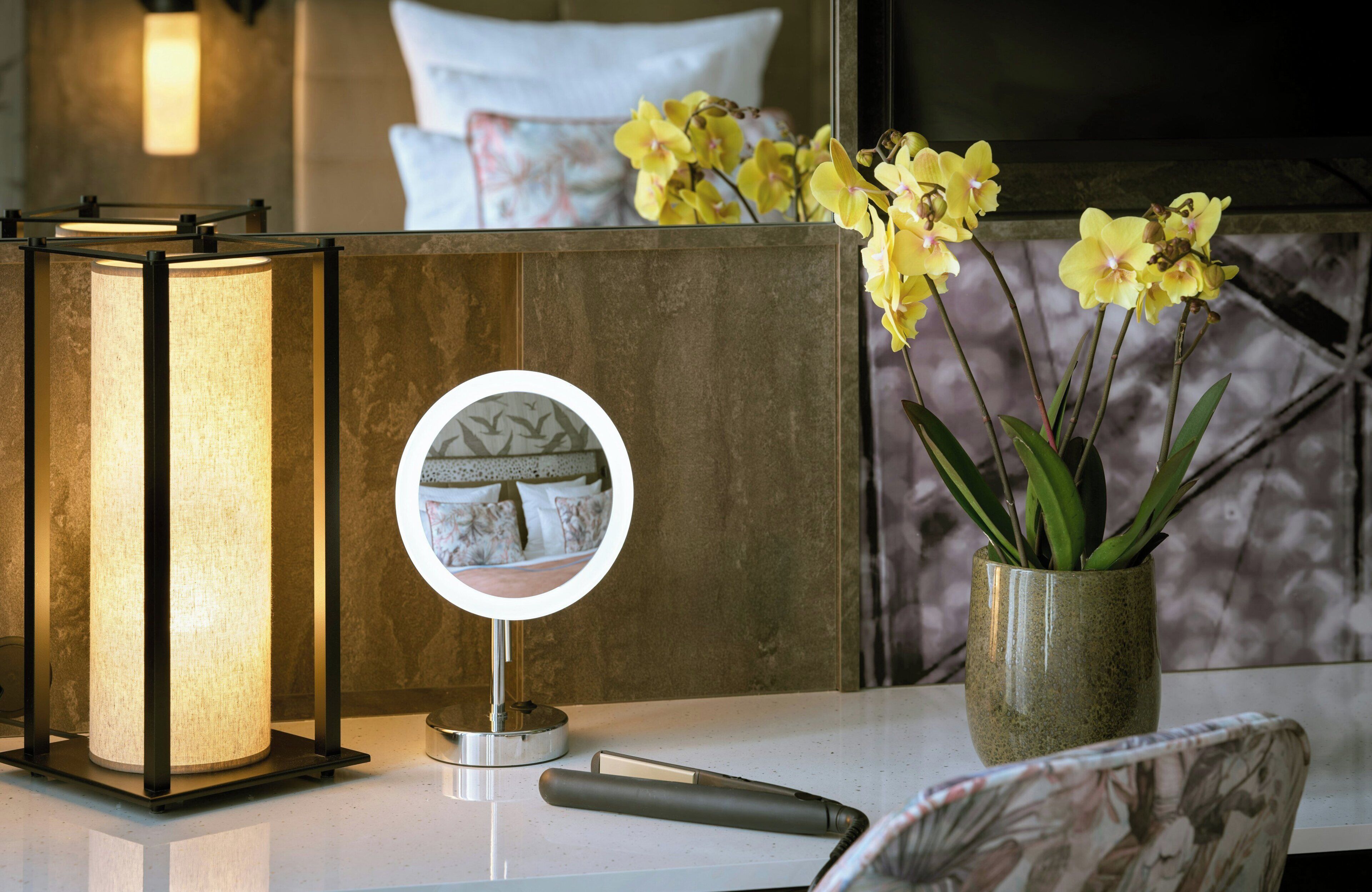 Een moderne badkamer met een spiegel, een lamp en een vaas met bloemen.