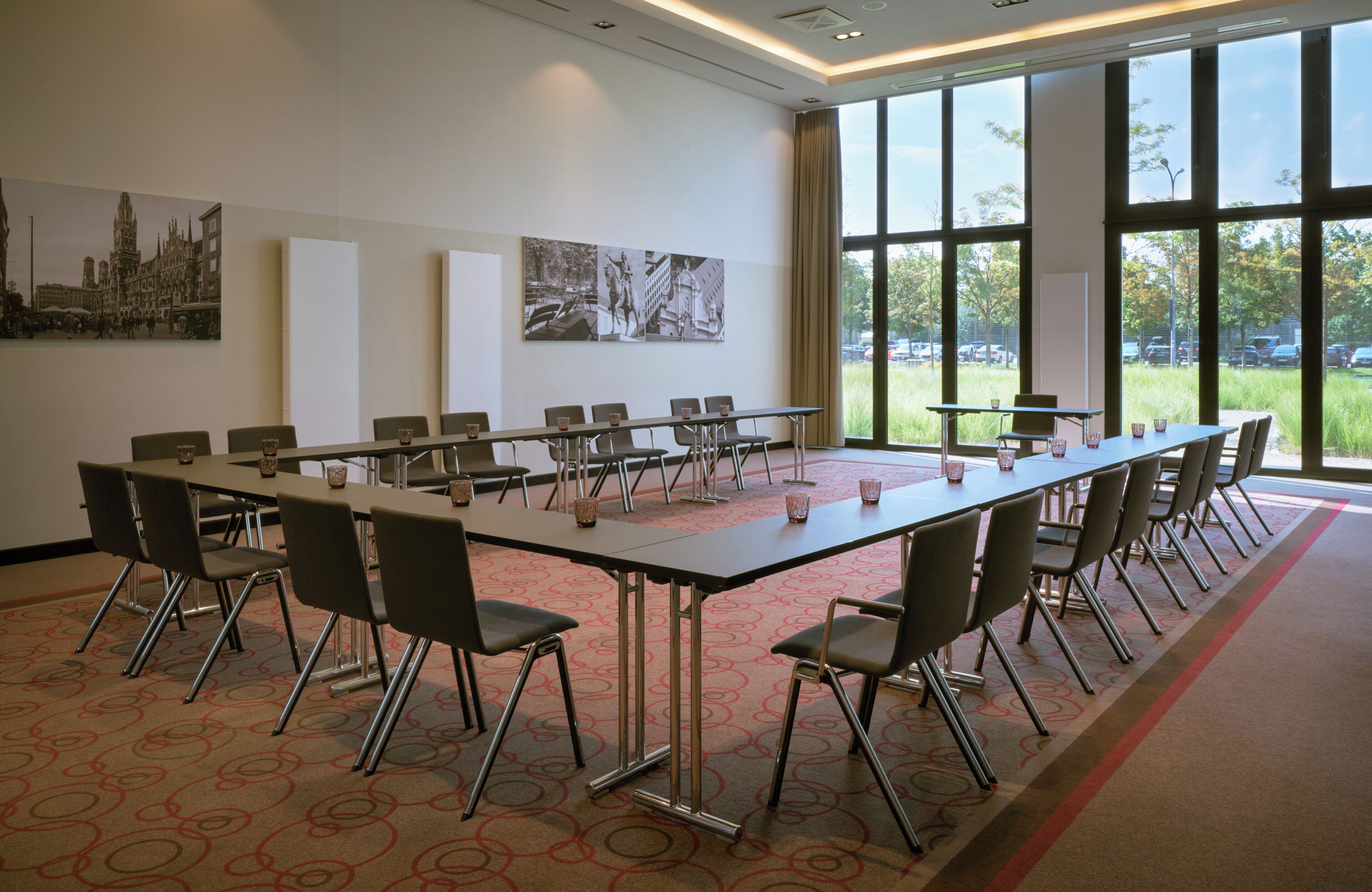 A conference room with a long table, chairs, and large windows offering a view of the outdoors.