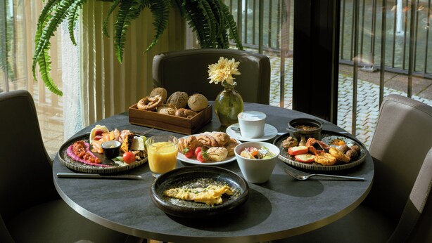 A breakfast table with various dishes, a coffee cup, and a vase with flowers. - Leonardo Royal Hotel Munich (Munich)