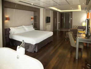 Une chambre d’hôtel moderne dotée d’un grand lit, d’un bureau avec un ordinateur, d’une chaise, d’une télévision et d’une salle de bain avec baignoire.