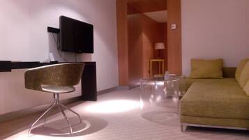 A modern hotel room with a sofa, a chair, a TV, and a small table.