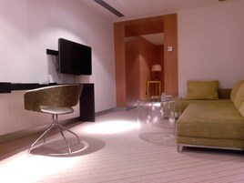 Une chambre d’hôtel moderne équipée d’un canapé, d’un fauteuil, d’une télévision et d’une petite table.