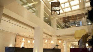 Un moderno vestíbulo de hotel con una recepción, techos altos y una barandilla de vidrio que da a un nivel inferior.