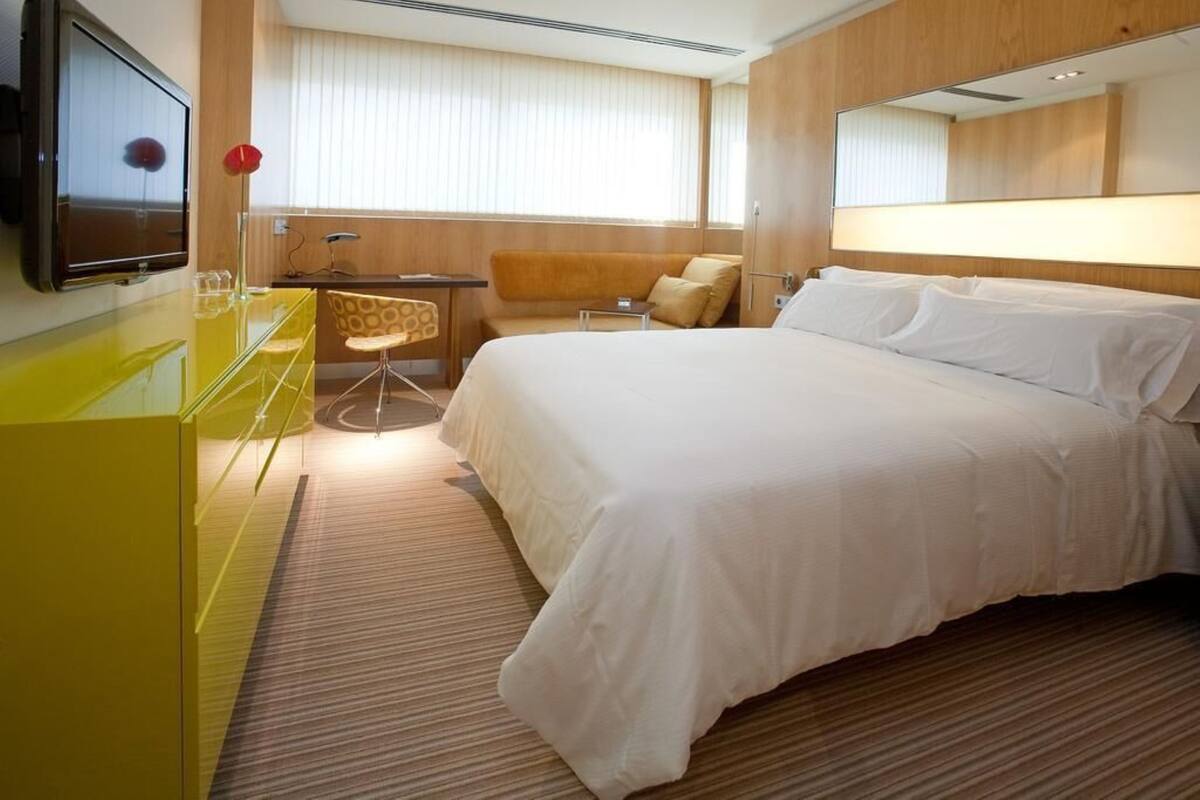 A hotel room with a bed, a desk, a chair, a TV, and a mirror.