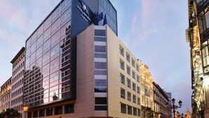 Un hotel moderno con fachada de vidrio, un logotipo destacado y ubicación en esquina con vistas a la calle.