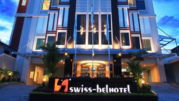Un hotel moderno con una entrada destacada, un letrero que dice "Swiss-Belhotel" y un cielo despejado al fondo.
