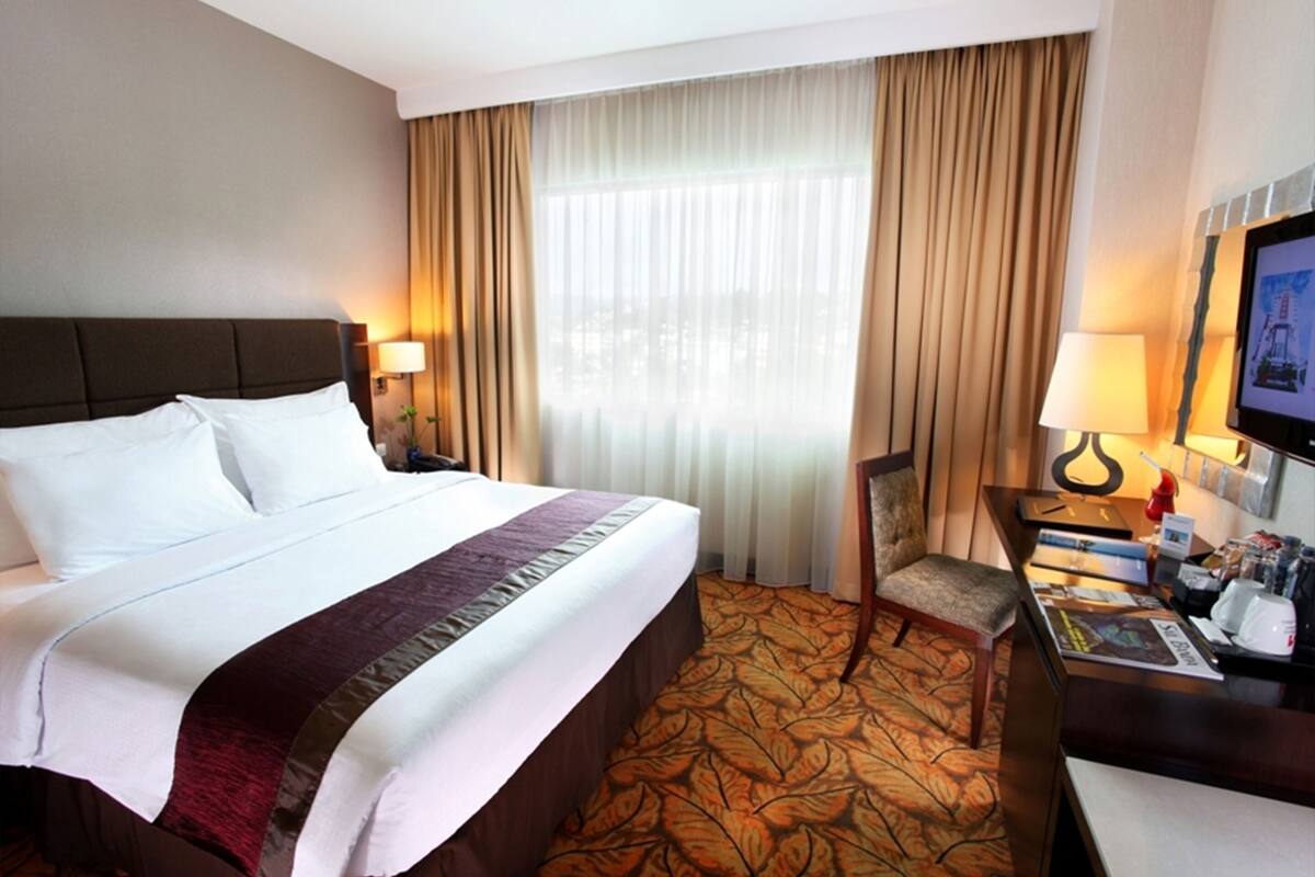 A hotel room with a large bed, a desk, a chair, and a television.