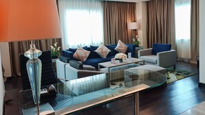 Una habitación de hotel moderna con una mesa de centro de vidrio, un conjunto de sofás, una silla y una lámpara.