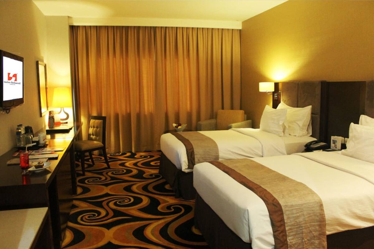 A hotel room with two beds, a desk with a chair, a lamp, and a television.
