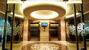 Un vestíbulo con un diseño circular central, dos ascensores y una pantalla de televisión.