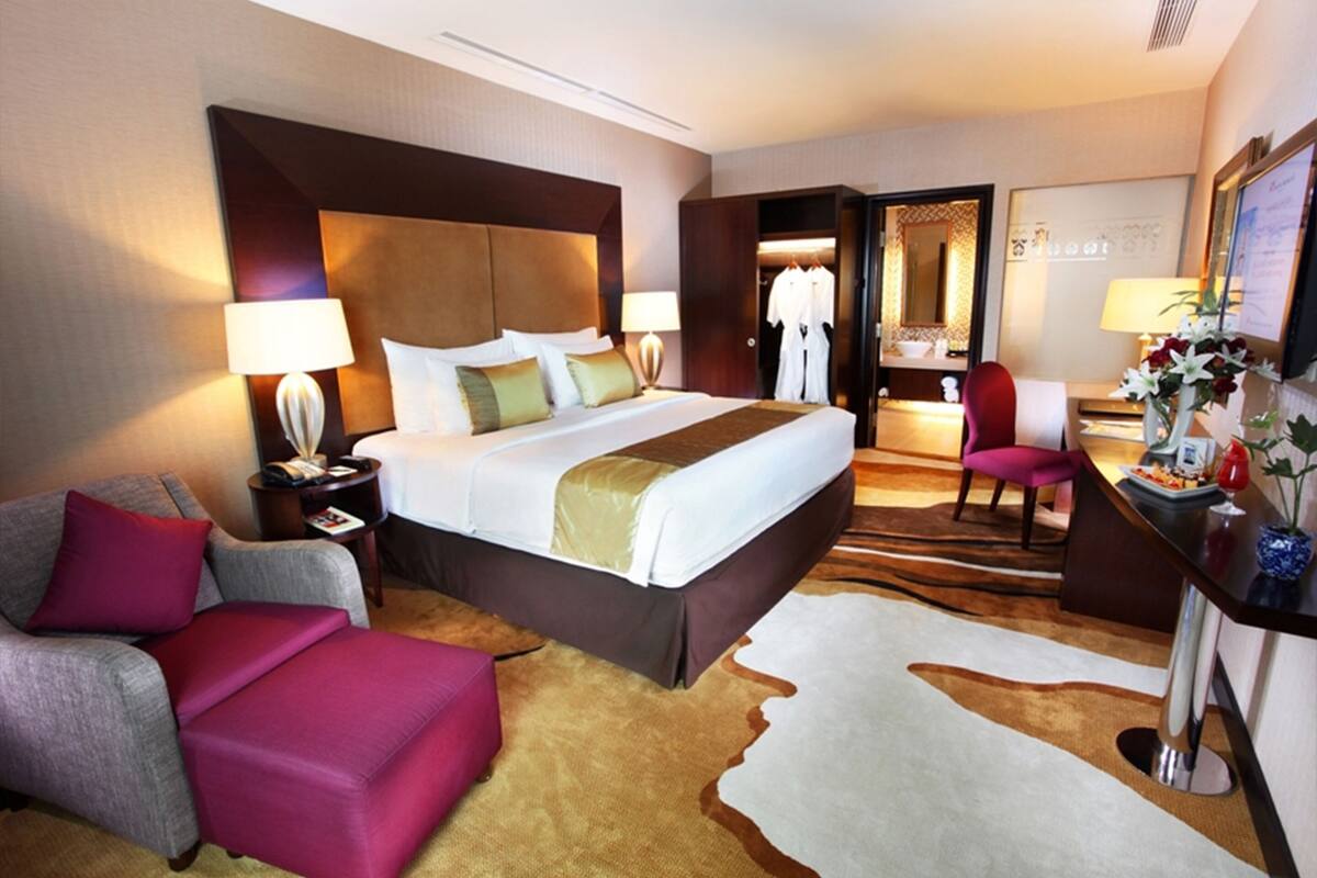 A hotel room with a large bed, a desk with a chair, a sofa, and a mirror.