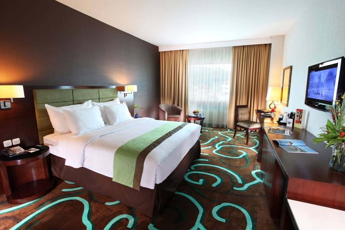 A hotel room with a large bed, a desk with a TV, a chair, and a window with curtains.