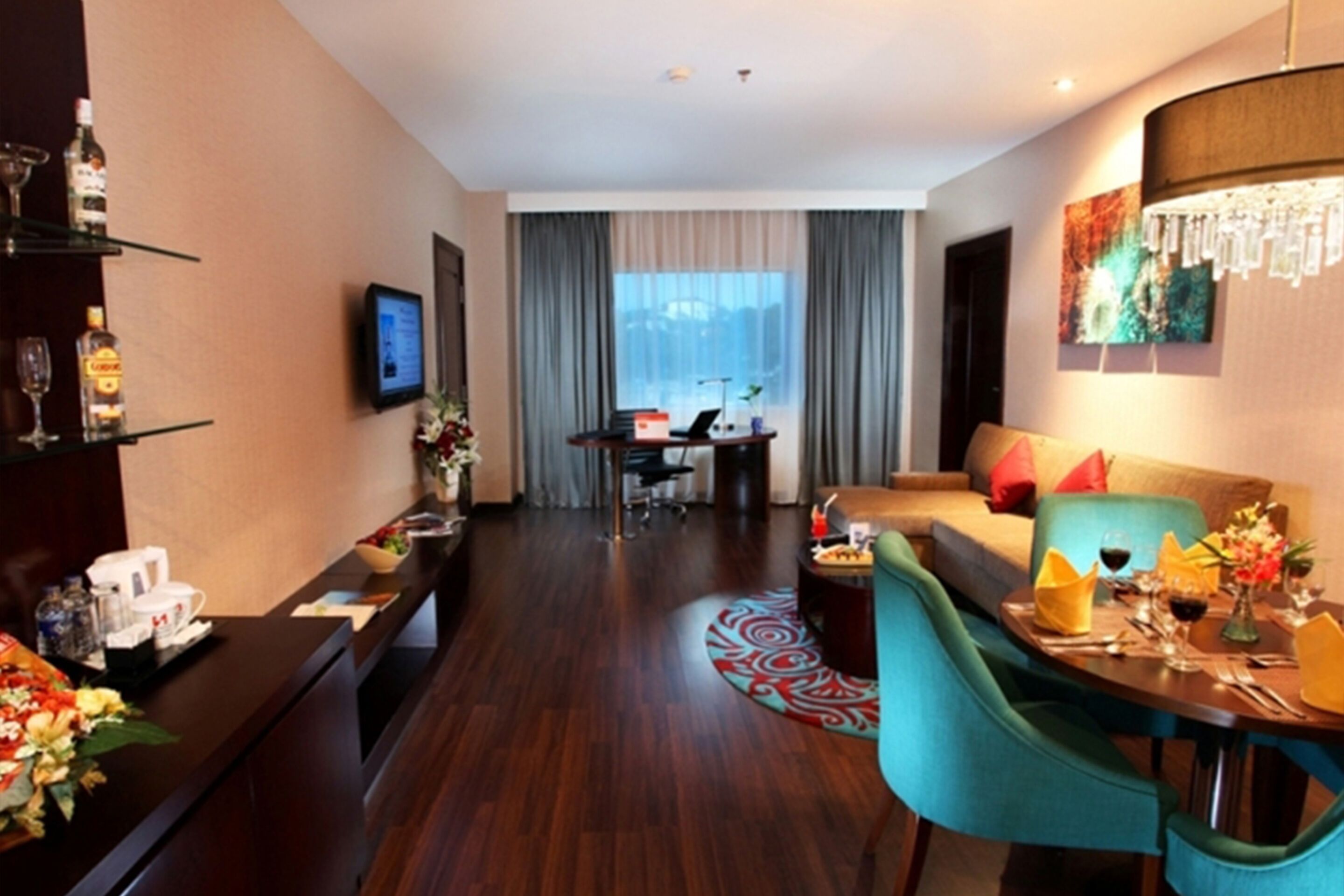 Ein Hotelzimmer mit Holzboden, einer Couch, einem Esstisch mit Stühlen, einem Schreibtisch mit Computer und einem an der Wand befestigten Fernseher.