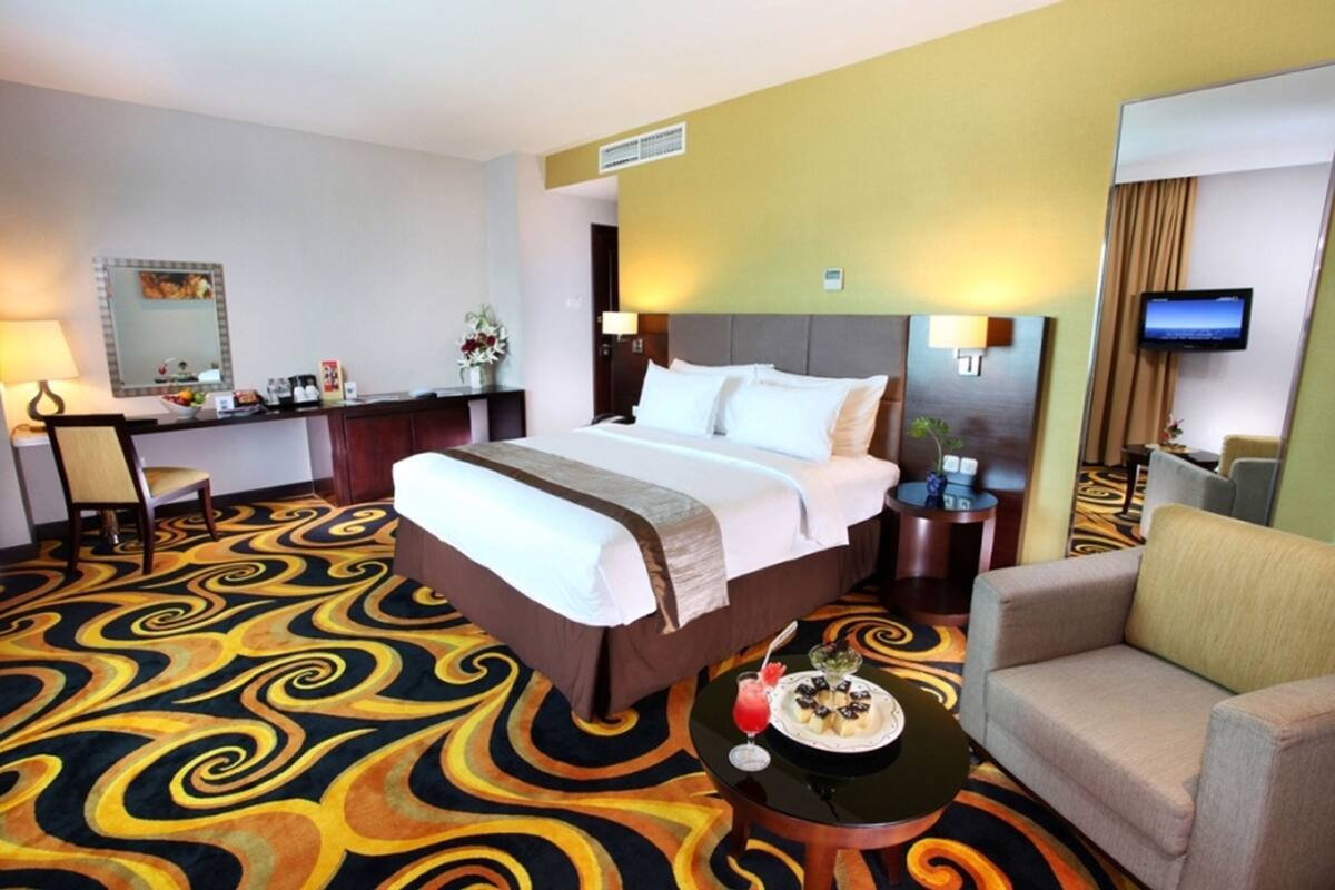A hotel room with a large bed, a desk with a chair, a TV, and a sofa.