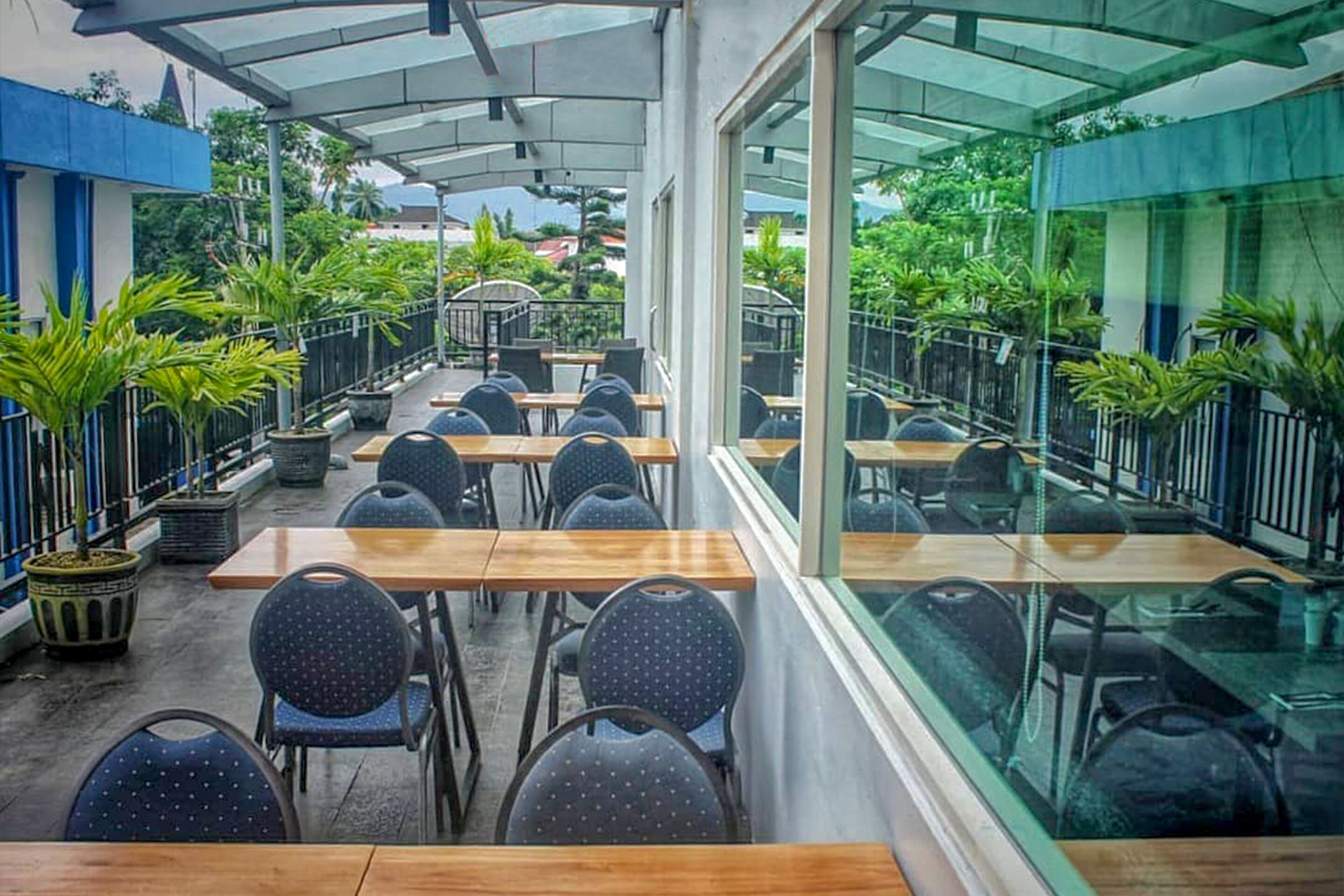 An outdoor café with tables and chairs, surrounded by potted plants and glass railings.