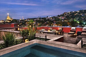 Zona de piscina en la azotea con mesa y sillas, rodeada de plantas y una cerca decorativa.