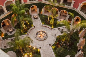 Un patio central con una fuente, rodeado de palmeras y zonas de estar, con senderos y arcos de piedra.