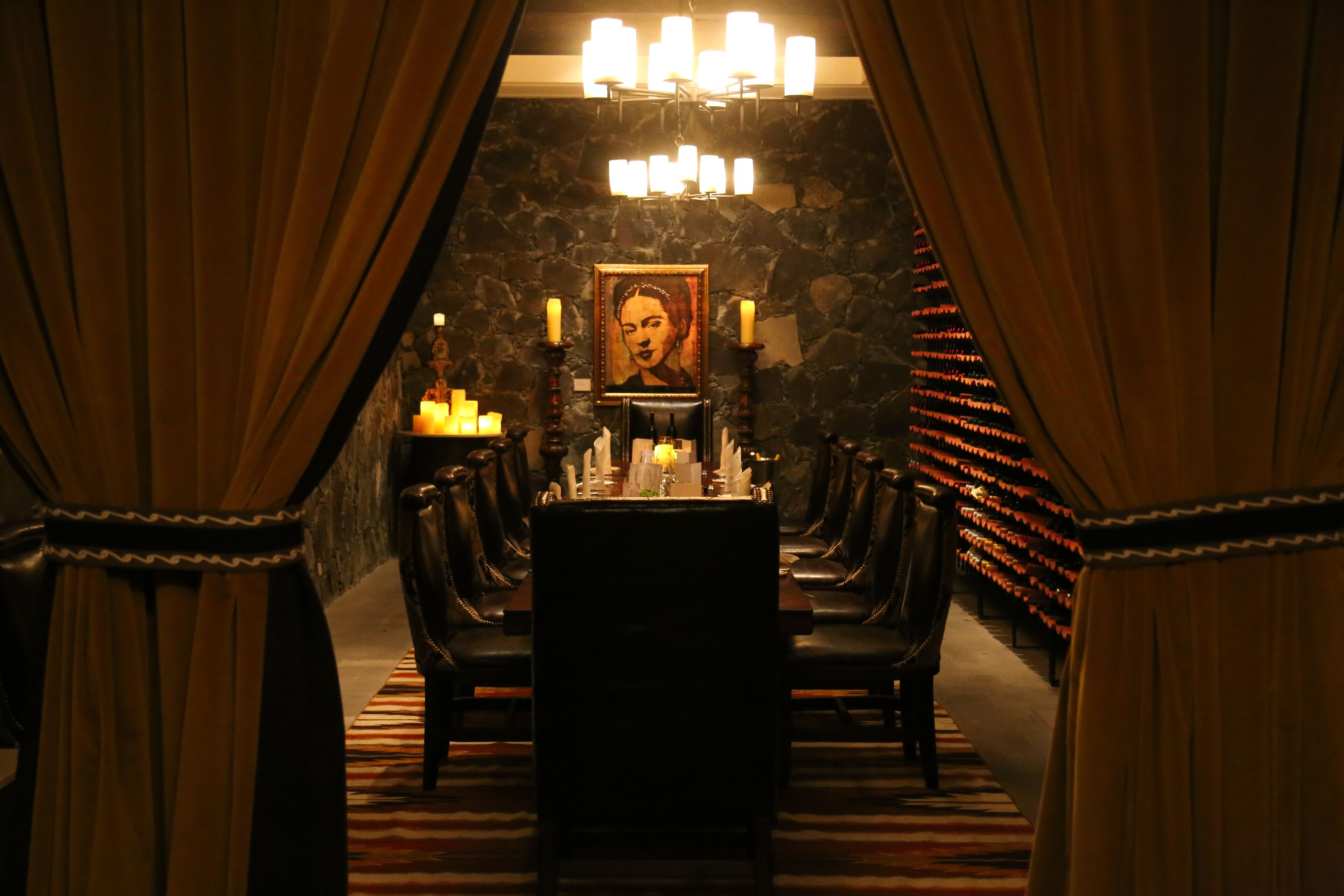 Uma sala de jantar com iluminação suave, com uma mesa posta para quatro pessoas, acompanhada por cadeiras de couro, um candelabro e velas. Um retrato emoldurado está pendurado na parede.
