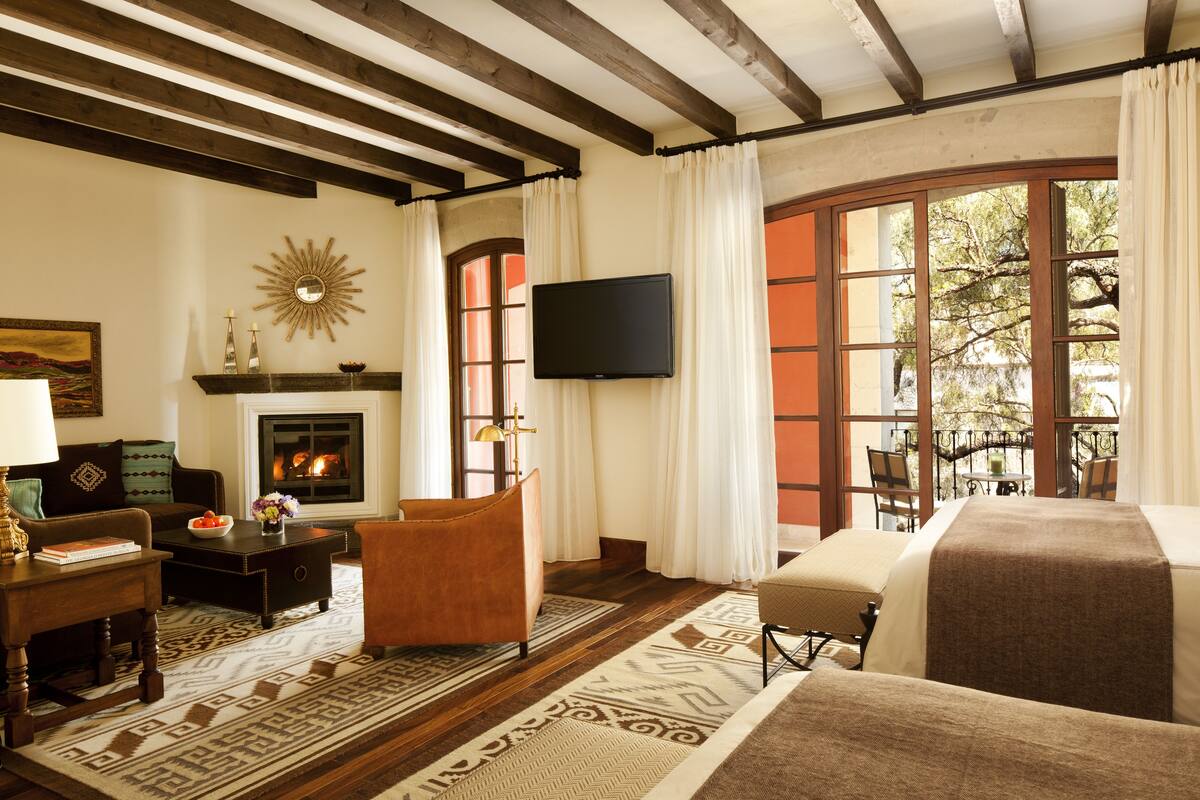 A cozy living room with a fireplace, a television mounted on the wall, and a large window with curtains.