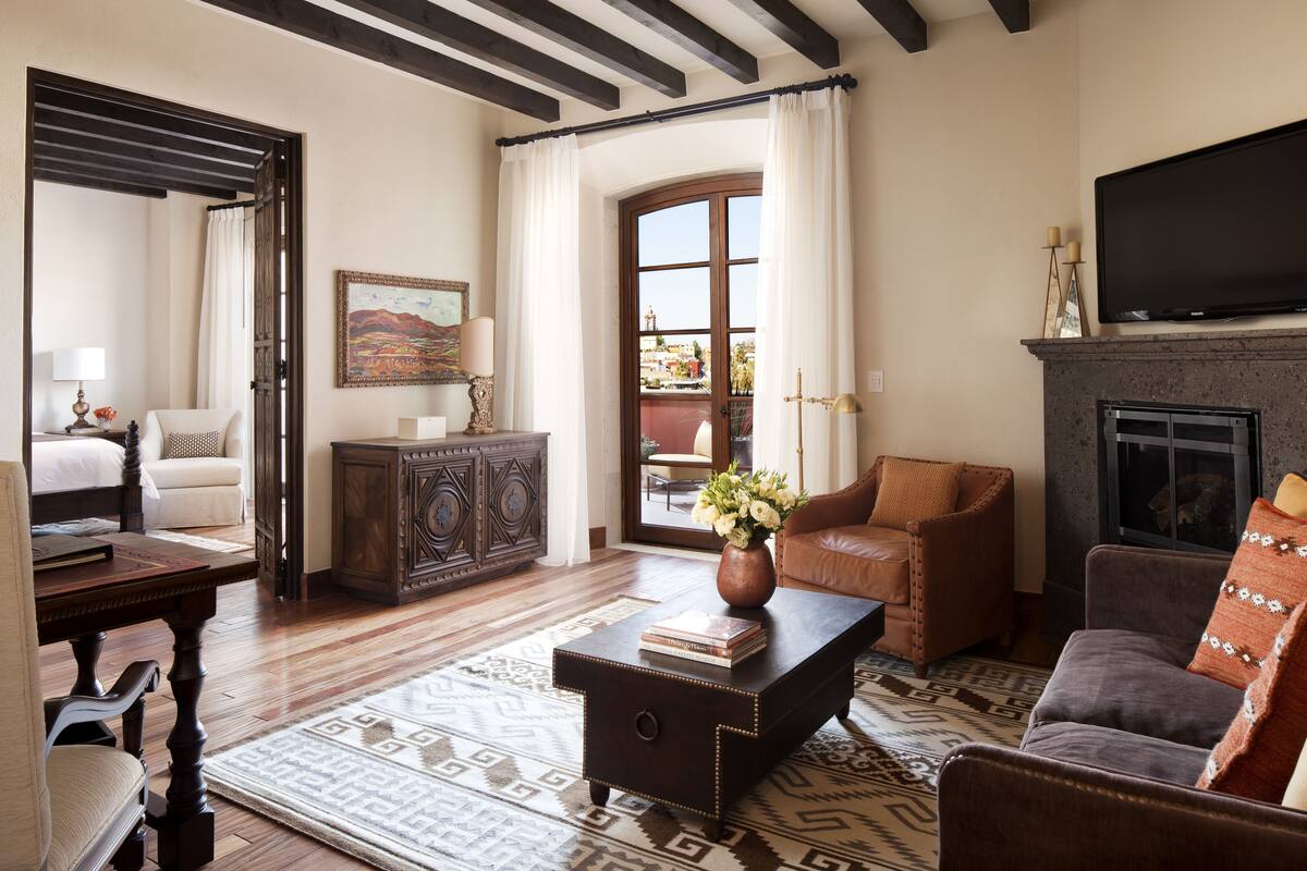 A living room with a fireplace, a sofa, a coffee table with books, a side table, and a view through a doorway to an outdoor area.