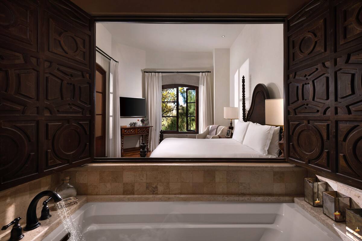 A modern bathroom with a large bathtub, a vanity with a mirror, and a window with curtains.