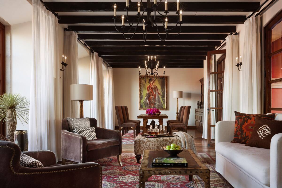 A spacious living room with a chandelier, leather sofas, a coffee table, and a dining area with a table set for two.