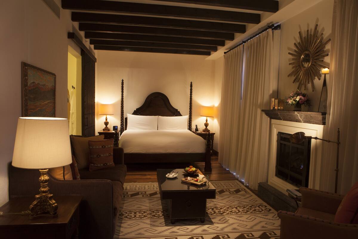 A hotel room with a large bed, a fireplace, a coffee table, and a desk with a lamp.