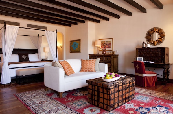 Un dormitorio con una cama con dosel, un sofá blanco, una mesa de centro de madera con fruta y una silla roja.